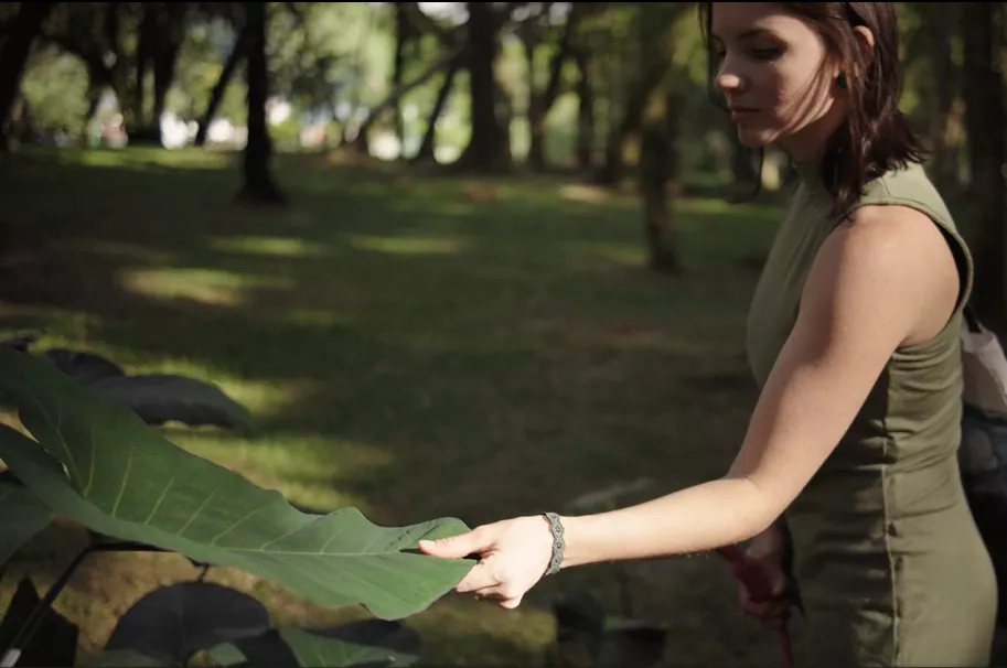 Mulher segurando uma folha verde grande, observando de perto em um parque