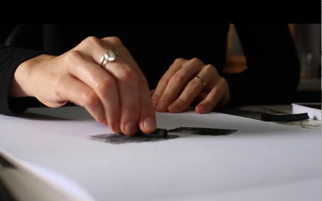Mãos apoiadas em uma folha de papel branco, no início de um desenho
